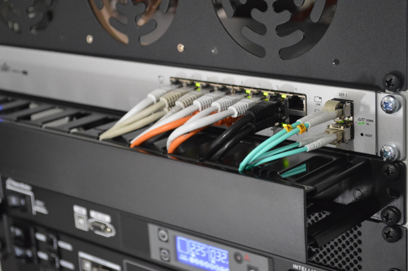 An image of a rackmount switch populated with cat6 and fibre, underneeth is a cable tray followed by a server